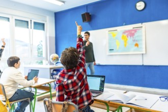 Elementary school student raising hand to answer a question in geography class, with teacher and