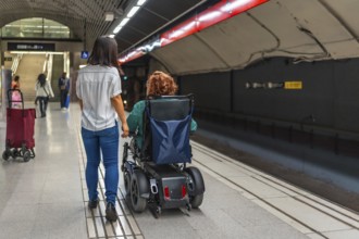 Rear view of a disabled caucasian adult woman in wheelchair and asian friend walking along metro