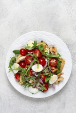A warm salad with fried chicken fillet, arugula and cherry tomatoes, and boiled quail eggs, on a