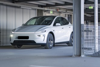 White electric car with modern lines and LED lights in a multi-storey car park, Tesla New Model Y