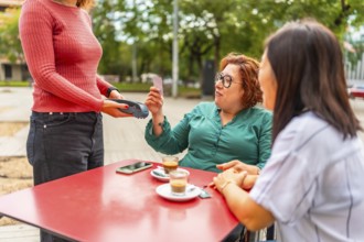 Woman with disability in wheelchair and friend paying with contactless in an outdoor cafeteria
