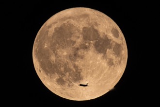 An aeroplane flies past in front of the so-called super full moon in August, Frankfurt, Hesse,