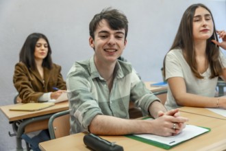 Portrait of a cheerful male student sitting at desk in classroom, attending a lesson at high