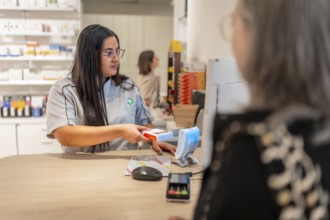 Pharmacist checking the price of a product attending a client in the counter of a modern pharmacy