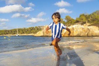 Happy child running on the wet sand of s'amarador beach in mallorca, spain, during summer holidays,