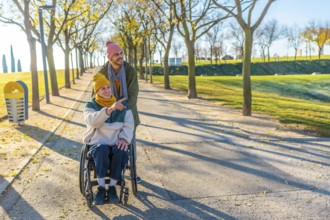 Happy friends enjoying a sunny autumn day together outdoors in a park, one pushing a wheelchair and