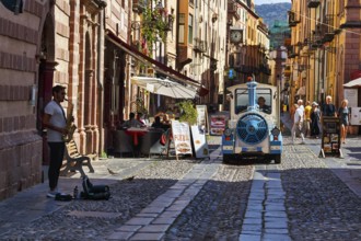 Trolleybus, street musicians, pedestrians and tourists in the picturesque old town of Bosa,