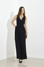 Cute lovely young woman in long sleeveless dress walking in bright room