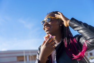 Low angle view photo of an african woman eating a multicolored doughnut in the street