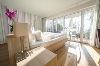 Modern, bright bedroom with wooden floor, large windows and a purple flower on the bedside table,