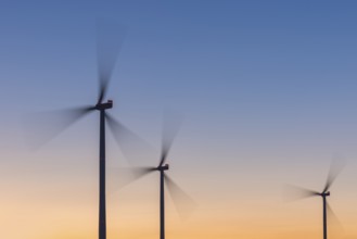 Three wind turbines in front of a colourful sky at sunset, moving quickly in the wind, Rems Valley,