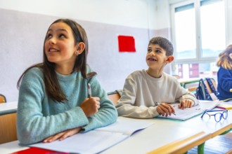 Two young pupils listening to their teacher in elementary school classroom during lesson, education