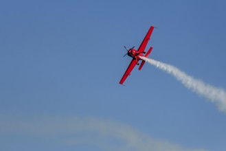 Red stunt aerobatic plane performing stunts in blue sky. Concept of speed, difficulty, precision,