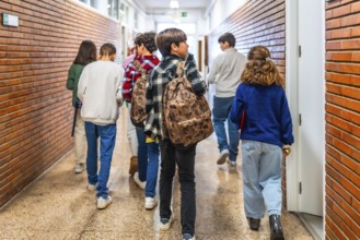 Group of elementary school students walking down school hallway between classes, carrying backpacks