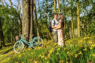 Romantic couple hugging in a forest full of daffodils with a bicycle parked nearby, enjoying a