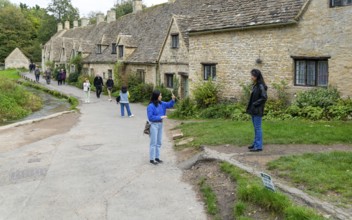 Tourists visiting famous Cotswold buildings at Arlington Row, Bibury, Gloucestershire, England, UK