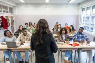 Female professor teaching a lesson to a multi ethnic group of students sitting at desks in a