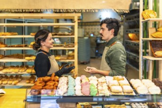 Side view of a male and female latin young workers of a bakery shop discussing in the counter