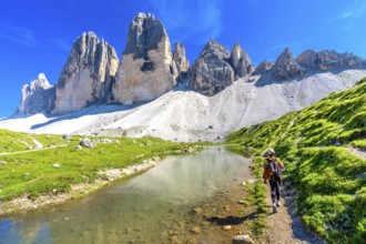 Tourist hiking along a scenic trail by a crystal clear alpine lake, with the stunning tre cime di