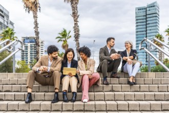 Multi-ethnic business people sitting in the street talking and using digital tablet together