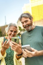 Vertical close-up photo of a caucasian happy modern senior couple using smartphone in the city