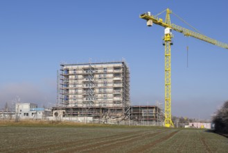 Unfinished building with yellow construction crane, construction site under blue sky, housing