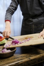 Unrecognizable man puts chopped red onions from a wooden cutting board in wooden bowl in the