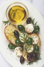 A plate with a snack, ciabatta bread with cheese and olives, olive oil, spices and herbs, top view,