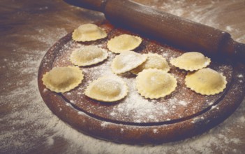 Fresh raw, uncooked ravioli, on a cutting board, with a rolling pin for dough, wooden background,