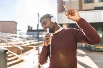 African man dancing listening to music with headphones in the city in a sunny day of autumn