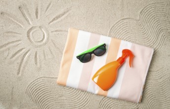 Drawing on the sand, sun and waves, sunglasses, with an orange bottle, beach towel, sun spray, on