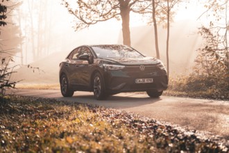 A Volkswagen on a country road in the morning sun mist between autumnal trees, electric car VW ID5,