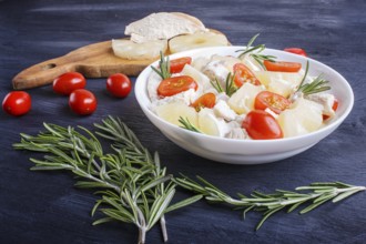Chicken fillet salad with rosemary, pineapple and cherry tomatoes on dark blue wooden background.
