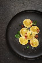 Fresh ravioli, with butter, spices and herbs, fried bacon, on a black plate, top view, dark