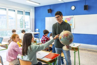 Geography teacher engaging students by pointing out countries on a globe during an interactive
