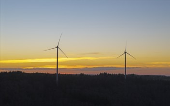Two wind turbines in front of a glowing sunset sky over a wooded landscape, Baden-Württemberg,