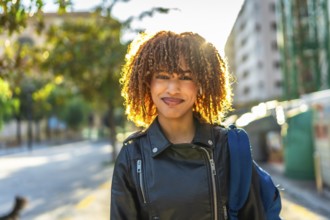 Confident young latin woman with curly hair and leather jacket smiling at camera standing in the