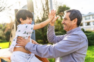 Grandfather and grandson are enjoying time together at the playground, giving a high five and