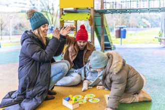 Parents and children having fun together playing a board game on a playground during winter