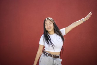 Frontal portrait of a happy beauty young asian woman raising arm dancing K-pop against a red urban