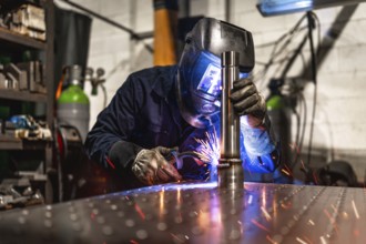 Concentrated male worker wearing protective gloves and facial mask welding in a metal factory alone