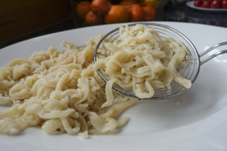 Swabian cuisine, preparation of spaetzle, hand-scraped spaetzle, on serving platter, slotted spoon,