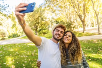 Frontal view of a young caucasian couple taking selfie standing in a park in a sunny day of spring