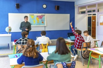 Group of teenage students raising hand and following geography lesson in classroom with teacher and