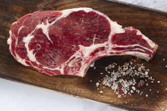 Raw rib eye steak, cowboy steak, wooden chopping board, marble table, top view, no people