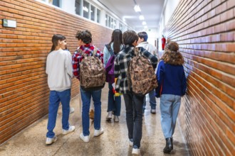 Rear view of diverse group of students walking down school hallway between classes, carrying