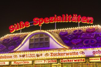 Candy stall flooded with light at a funfair at night, decorated with traditional treats,