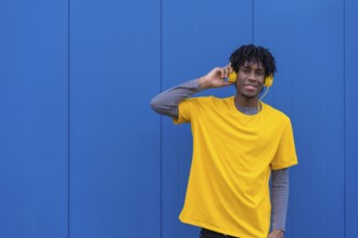 African young man listening to music with headphones next to a blue wall