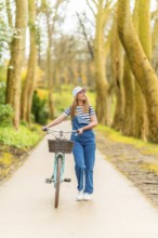 Young woman walking with her vintage bicycle in a beautiful tree lined path, enjoying a sunny