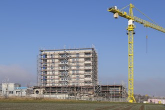 Incomplete building with yellow construction crane in clear sky, housing construction, new